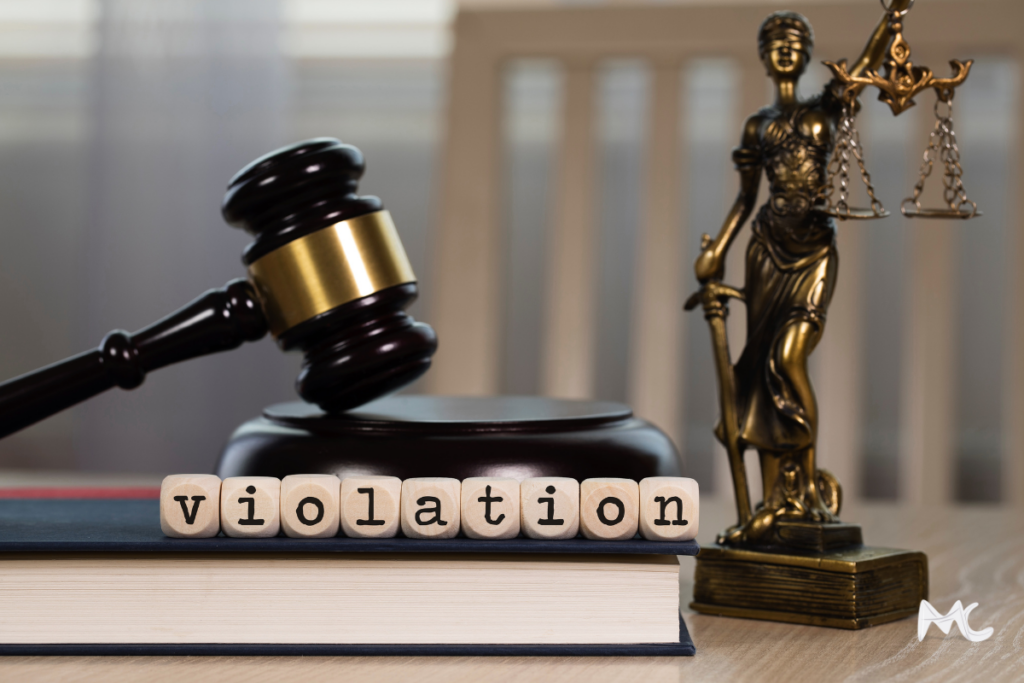 A gavel and scales of justice statue in front of a sign reading 'violations.'