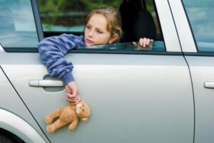A minor girl in a car looking out the car holding a teddy bear.