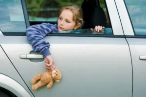 A minor girl in a car looking out the car holding a teddy bear.